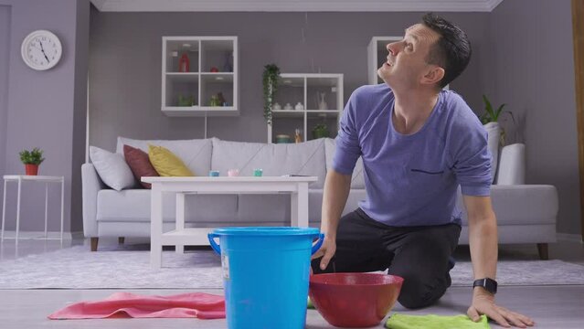 Man holding bucket under leaky ceiling and mopping floors.
Sad man waiting for roof repair service looking at water falling from ceiling into plastic buckets.
