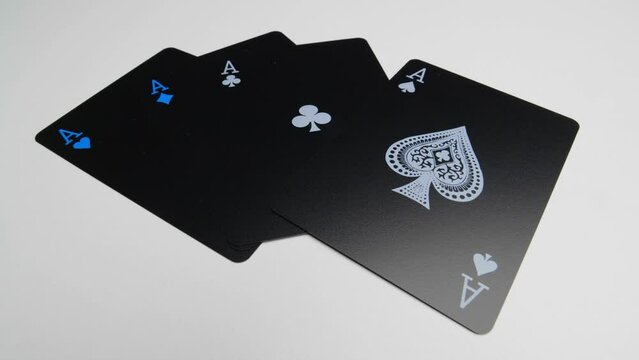 Orbit shot of the four aces on a white surface of a deck of black cards