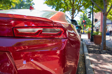 a tail light on a red Ford Mustang parked on the street surrounded by lush green trees in Atlanta...
