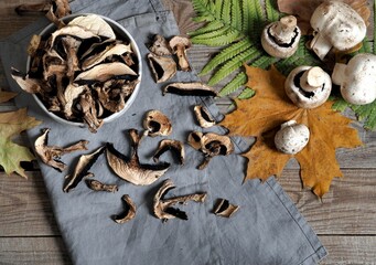 Autumn wooden background. Dried and fresh champignon mushrooms in a bowl and on a cutting kitchen board. The idea of natural organic ecological products .