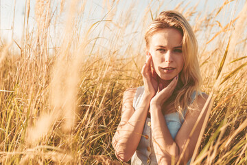 Beautiful blonde woman on a walk in a field with dry grass. A walk in nature, sunset in a field of...