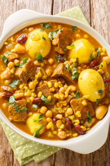Cholent or hamin is a traditional Jewish stew made of meat, potatoes, mix beans and barley closeup in the pan on the table. Vertical top view from above