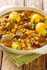 Cholent or hamin is a traditional Jewish stew made of meat, potatoes, mix beans and barley closeup in the pan on the table. Vertical