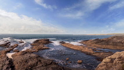 Fototapeta premium Rough stone coast line and powerful waves in the ocean. Spanish point part of Wild Atlantic Way tourist route, county Clare, Ireland. Warm sunny day, blue cloudy sky and water. Irish seascape.