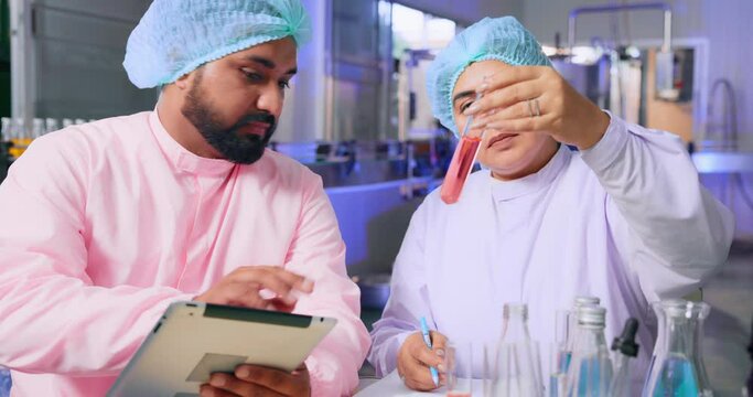 In An Industrial Water Factory, A Food Scientist Worker Wearing A Hairnet And A Face Mask Converses While Monitoring Quality Control And Putting Comments On Juice Bottles. Beverage Line Inspection