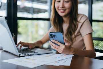 Freelancer beautiful asian woman success business project with mobile phone and digital laptop computer happy and relax at workspace in the evening near windows.