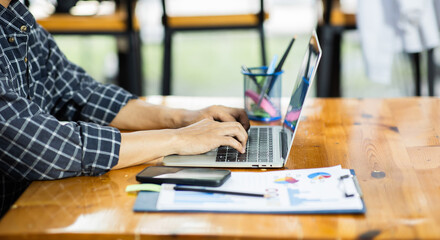 Close-up photo of a business man or accountant working on his laptop computer with business documents, graphs and calculators on his desk.