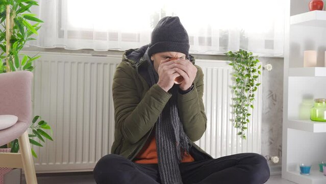 A cold man in a cold apartment.
Man in thick clothes feels cold at home and leans on combi boiler.
