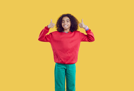 Happy African American Pretten Girl On Yellow Background Showing Thumbs Up Recommending Best Choice. Portrait Of Positive Cute Curly Ethnic Teen Girl Dressed In Casual Clothes Showing Two Thumbs Up.