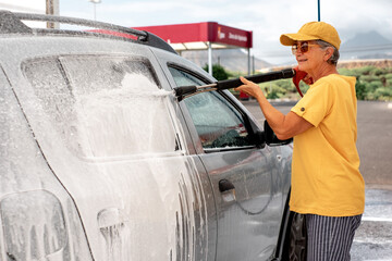 Smiling caucasian senior woman washing her car in a self-service car wash station using high...