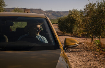 Adult man in cowboy hat driving car in olive grove, Almeria, Spain