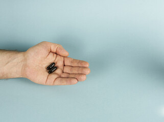 There are two black capsules on the man's palm. Concept - vitamins for men.

