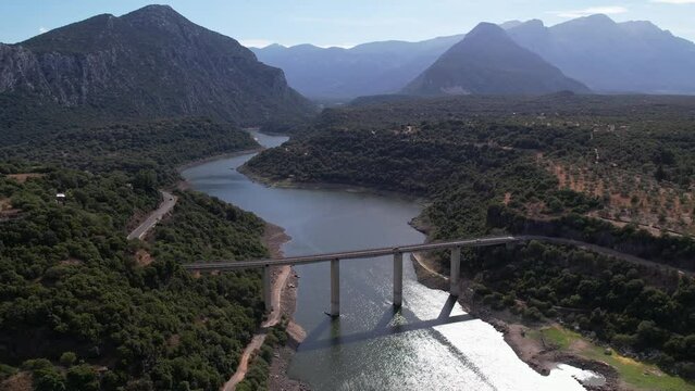 Aerial View Of Strada Provinciale 38 Road Crossing River Lago del Cedrino With Mountain Landscape In The Background. Parallax Shot