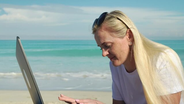 successful business woman making money on beautiful sandy beach, she works and travels. Pretty blond model with a notebook or laptop relaxing on vacation smilling enjoying life.