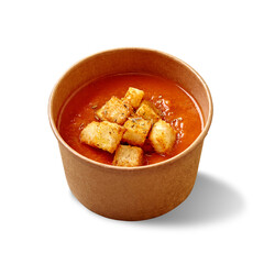 Cardboard bowl of cold tomato gazpacho with croutons and dried herbs isolated on white