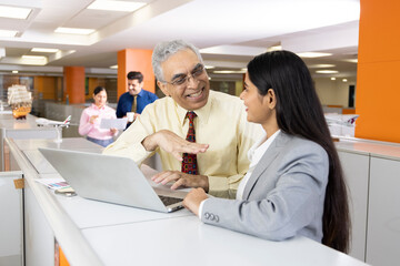 Senior businessman with woman using laptop at office.