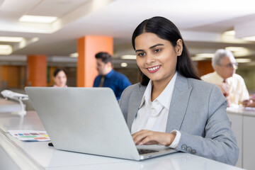 Happy indian businesswoman using laptop in office