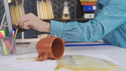 Office worker spills coffee on documents.
Office worker accidentally hits coffee mug and spilled coffee wets the paper.
