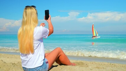 Girl vlogger on the beach. Caucasian woman on the sea beach shoots a video from a smartphone for the Internet and social networks - Powered by Adobe