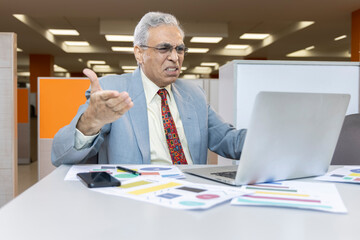 Displeased senior man using laptop at office.