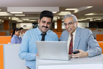 Happy mature businessman and his young assistant working in office.