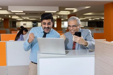 Happy mature businessman and his young assistant working in office.