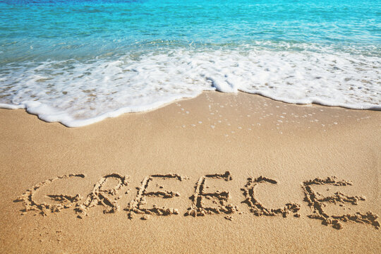 Inscription GREECE on a sandy beach with sea waves. Nature background