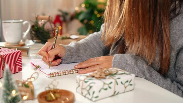 Goals plans make to do and wish list for new year christmas concept, girl writing in notebook. Woman hand holding pen on notepad at home on winter holidays xmas. Christmas decoration, gift boxes. 
