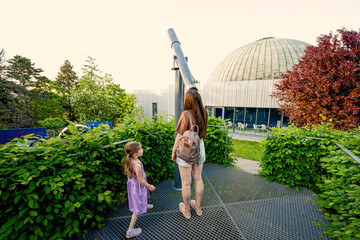 Mother with daughter at observatory looking in telescope outdoor.
