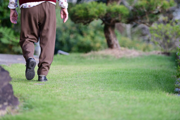 芝生の庭を一人で散歩するシニア女性の後ろ姿