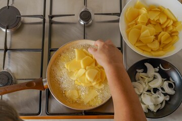 woman's arm pouring potatoes into a pan with boiling oil - Powered by Adobe