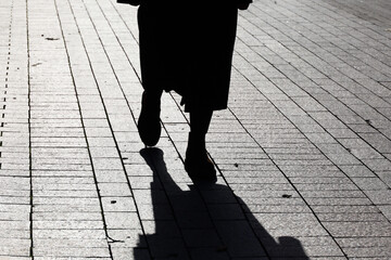 Silhouette of lonely woman in autumn clothes walking down the street, black shadow on pavement....