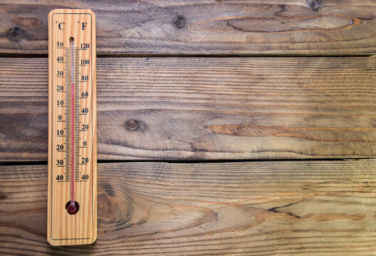 On a wooden wall hangs a wooden mercury thermometer at around 25 with a scale from minus 40 to plus 50 degrees near zero. Air temperature in the room. 25 degrees Celsius or 80 degrees Fahrenheit.