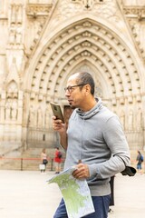 Latin man talking on his cell phone and map in his hand in front of the Cathedral of Barcelona (Spain), vacation concept.