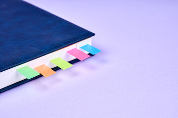 An office notepad with colorful sticky page markers sandwiched between pages on purple background