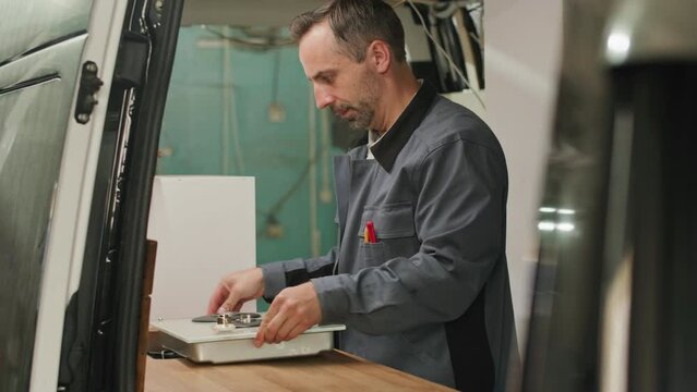 Middle aged Caucasian man bringing cooker while assembling kitchen in camper van
