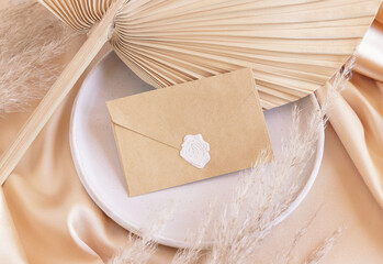 Sealed envelope on plate on dried palm leaf and beige silky fabric close up, mockup
