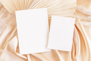 Blank cards on beige satin fabric and dried palm leaf close up, greeting or wedding mockup