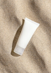 White cream tube on beige sand top view, hard light. Cosmetic packaging mockup