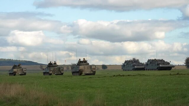 Several British army Warrior FV510 infantry fighting vehicles and Challenger CRARRVs in action over grass fields on a military exercise, Wiltshire UK
