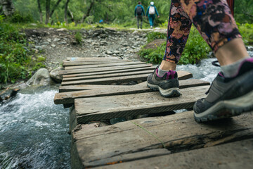 Woman wearing outdoor boots walking across a wooden bench crossing a wild mountain creek, close-up