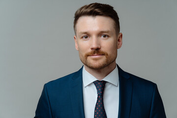 Serious confident businessman wears formal clothes looks directly at camera has well groomed appearance ready for meeting with partners isolated over grey studio background. Motivated entrepreneur