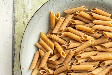 Uncooked whole grain pasta. Raw penne pasta in plate. Top view.