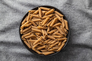 Uncooked whole grain pasta. Raw penne pasta in plate. Top view.