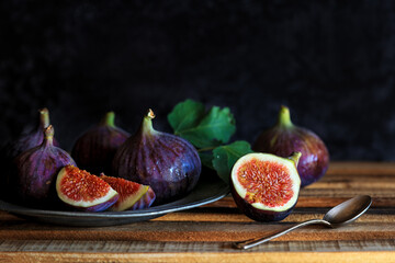 Fresh fig fruits in a vintage metal plate with cut pieces with a spoon against vintage background - dark and moody photography
