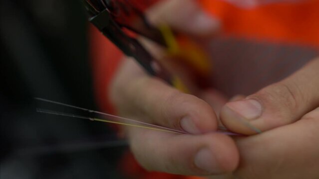 A close up shot of a technician is cutting fiber optic cables. Only his hands are visible along with the fiber optical and the cutter machine in this video  
