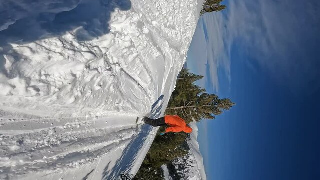 Vertical video of snowboarder in orange jacket freeriding through trees