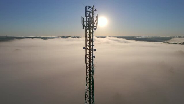 Aerial View of Tower Antenna Telecommunication Cell Phone, Radio Transmitters of Cellular 5g 4g Mobile Phone. Providing High Speed Modern 5g Traffic Network Service. Fog Clouds and Sky in Sunrise Time