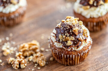 Tasty chocolate muffin with creme mascarpone and chocolate on top, covered with nuts. Placed on wooden desk. Sweet fresh and homemade cupcake.