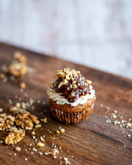 Tasty chocolate muffin with creme mascarpone and chocolate on top, covered with nuts. Placed on wooden desk. Sweet fresh and homemade cupcake.